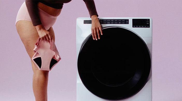 model holding bladder leak underwear in front of a washing machine