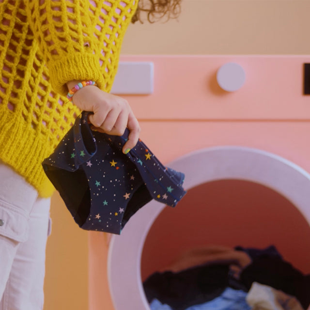 model holding period underwear in front of a washing machine