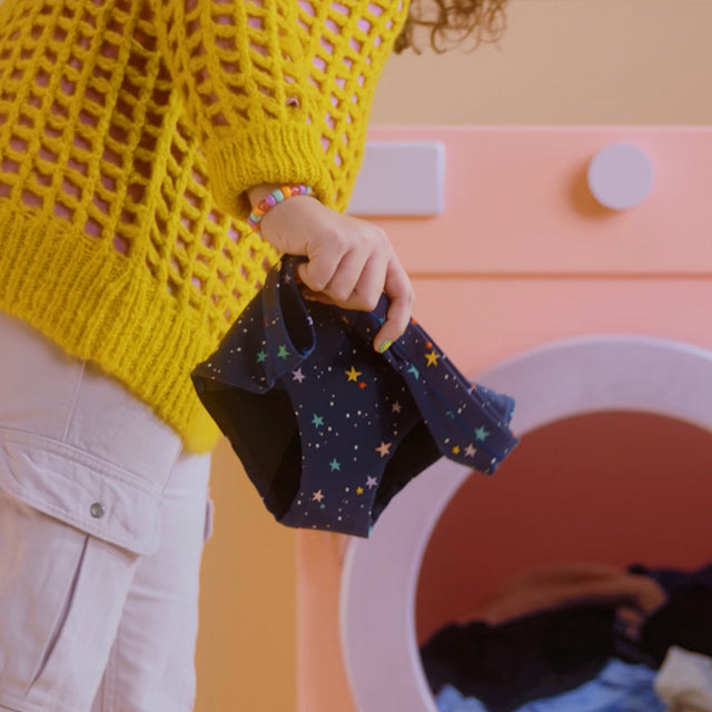 model holding teen period underwear in front of a washing machine